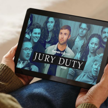 A person holiding an Amazon Fire HD 10 tablet showing the show Jury Duty