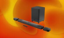 A multi-piece black, JBL soundbar appears on a swirly orange and yellow background.