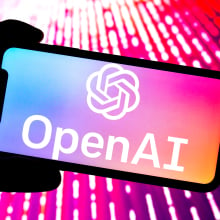 OpenAI logo open on a phone bathed in pink light. 