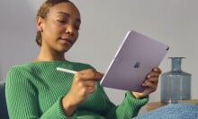 a person wearing jeans and a green sweater sits on a couch while using the apple ipad air with an apple pencil