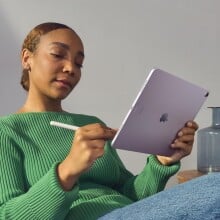 a person wearing jeans and a green sweater sits on a couch while using the apple ipad air with an apple pencil