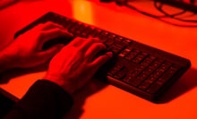 A hand typing on a keyboard bathed in red light. 