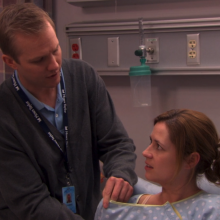 A male lactation nurse helping a woman who's sitting in a hospital bed.