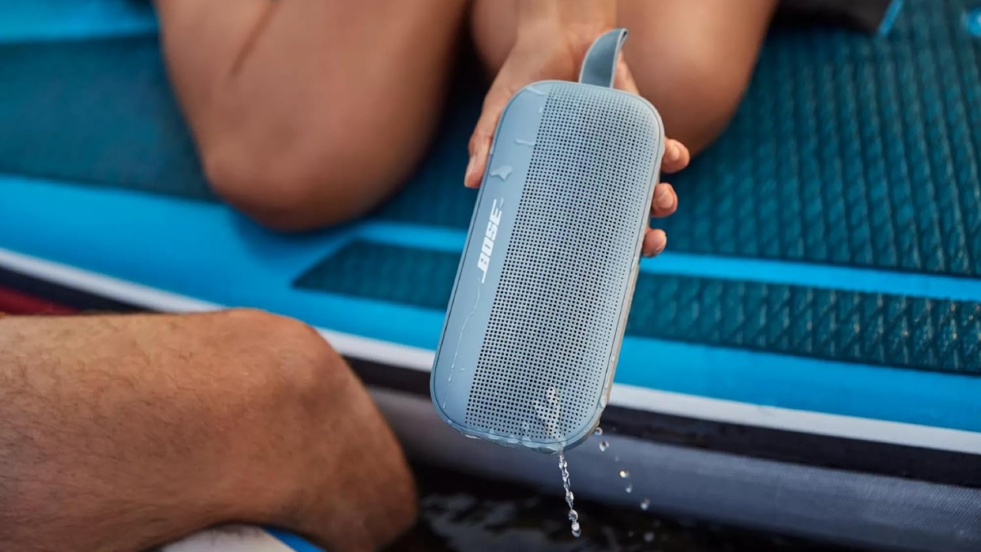 woman holding blue bose speaker dripping with water