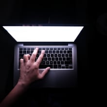 A hand hovers ominously over a keyboard against a dark background. 