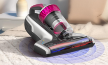 A pink and silver Jimmy WB73 mattress vacuum cleaner sits on a bed, with a graphic showing a blue light emanating from the vacuum head.