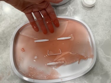 hand peeling pink jelly face mask off of its mold