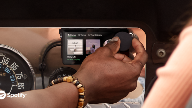 A hand turning a dial on a small Car Thing screen.