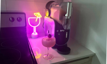 Glass of frosé on countertop beside Ninja Slushi machine with neon cocktail light in background