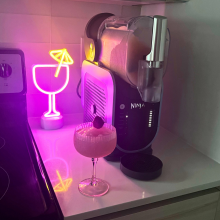 Glass of frosé on countertop beside Ninja Slushi machine with neon cocktail light in background