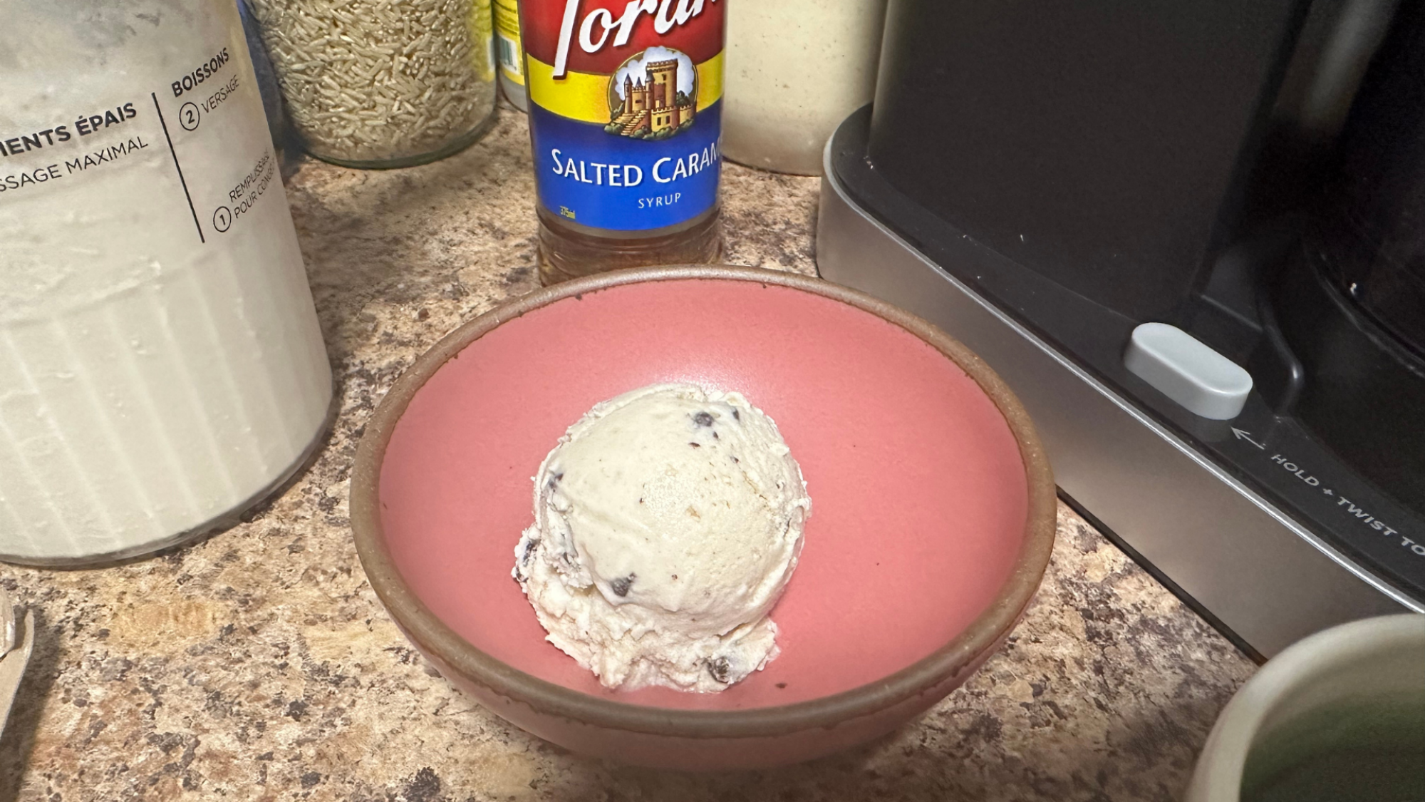 A scoop of ice cream in a pink ceramic bowl.