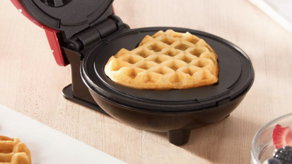 a red dash waffle maker filled with a heart-shaped waffle