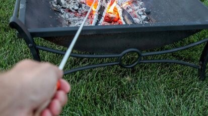 close-up view of person holding s'mores stick and marshmallow over fire pit