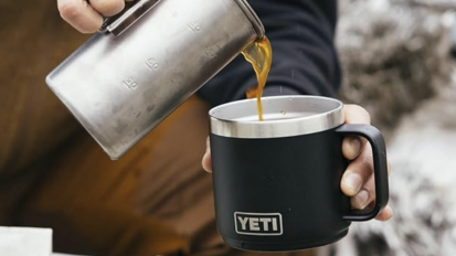 french press being poured into black yeti mug outdoors