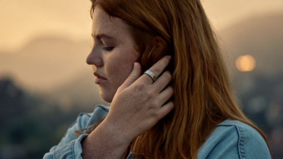 a woman tucking her hair behind her ear while wearing an oura fitenss ring