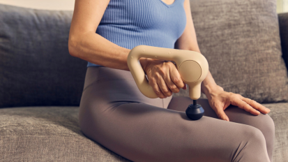 Person sitting on couch using Therabody massage gun on leg