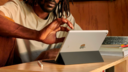 a close-up of a man scrolling on a 9th-generation apple ipad in tent mode while sitting at a wooden desk