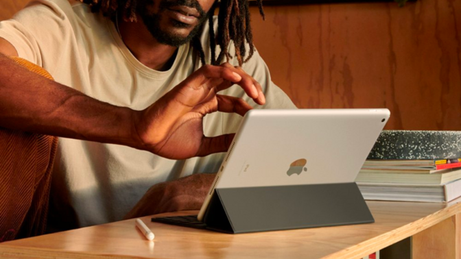 a close-up of a man scrolling on a 9th-generation apple ipad in tent mode while sitting at a wooden desk