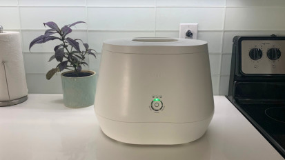 Lomi electric composter sitting on kitchen countertop with plant and paper towels in background