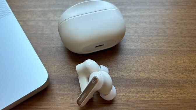 cream colored anker soundcore life p3i headphones and case next to laptop