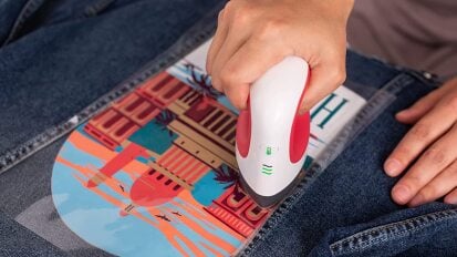 a close-up of a person using a cricut easypress mini to iron a decal onto a denim jacket