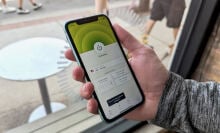 a close-up of a man holding an iphone displaying the expressvpn app in front of a window