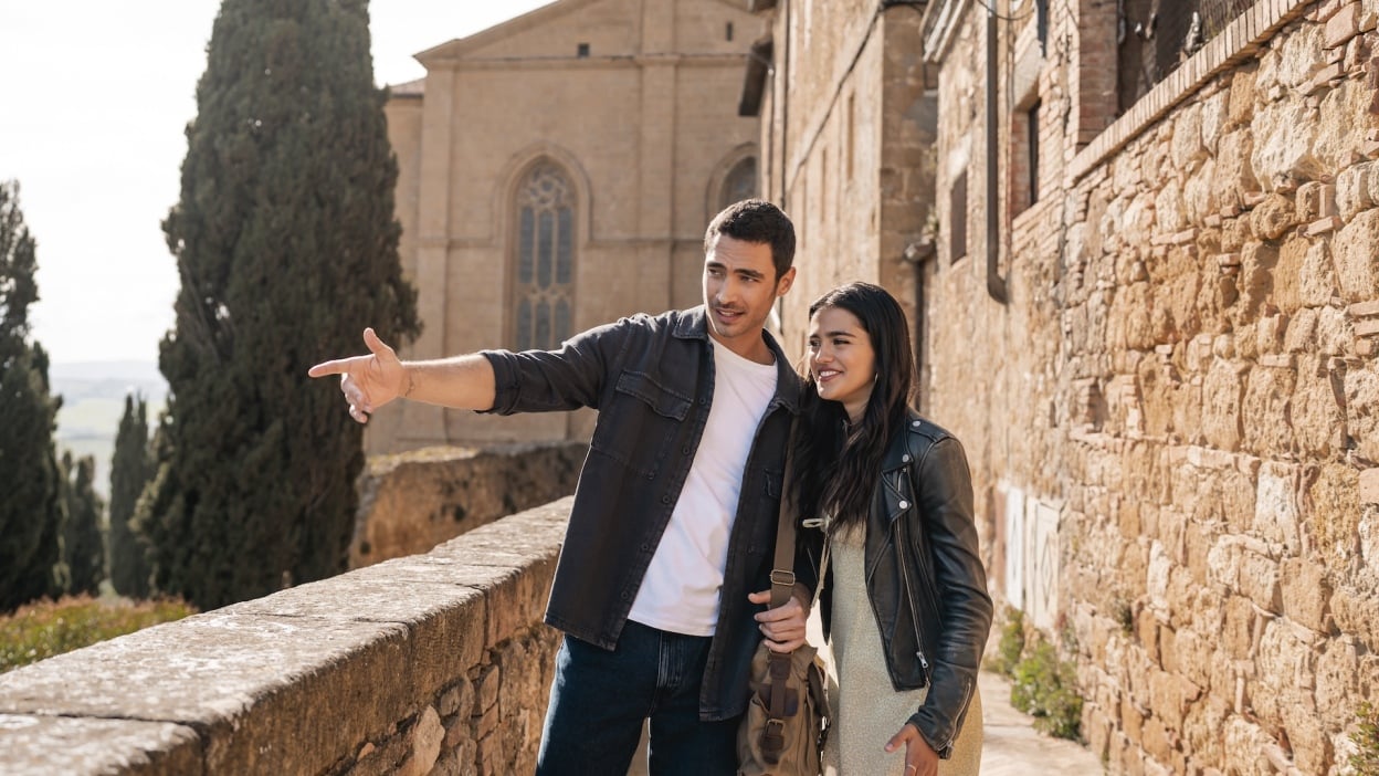 A young couple stand beside a Tuscan villa looking happy.