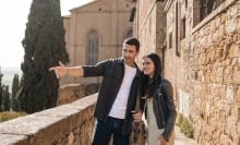 A young couple stand beside a Tuscan villa looking happy.