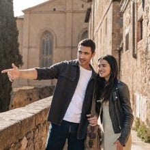 A young couple stand beside a Tuscan villa looking happy.