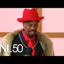 black man in black fur suit with red dress shirt and red fedora hat