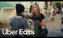 A young woman handing Jennifer Aniston a bag full of flowers.