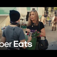 A young woman handing Jennifer Aniston a bag full of flowers.