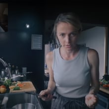 A woman seen on a video call stands in her kitchen holding a knife. In the top left is an image of her husband on the other end of the call.