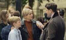 Jodie Whittaker stands in a scene from "Toxic Town" as a mother with her son talking to a reporter.