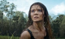 A dishevelled woman stands in a field, looking scared.