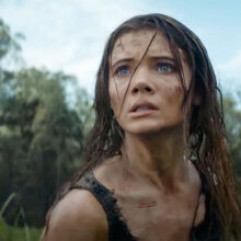 A dishevelled woman stands in a field, looking scared.