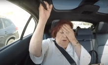 A woman sitting in the back seat of a car covers her face with one hand.