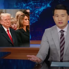 A man sits behind a talk show desk. An image in the top-left shows men and women in a church.