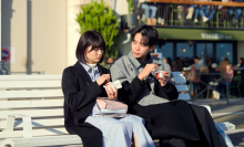 A still from 'Offline Love' showing a man and a woman eating ice cream on a bench. The man is looking at the woman, and the woman is looking at her ice cream.