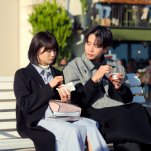 A still from 'Offline Love' showing a man and a woman eating ice cream on a bench. The man is looking at the woman, and the woman is looking at her ice cream.