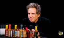 A man sits at a table covered in hot sauce in a dark room.