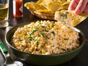 Creamy corn dip garnished with fresh herbs, served with tortilla chips and a beverage in the background. Creamy corn dip garnished with fresh herbs, served with tortilla chips and a beverage in the background.
