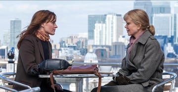 two women seated at an outdoor table with a city skyline in the background