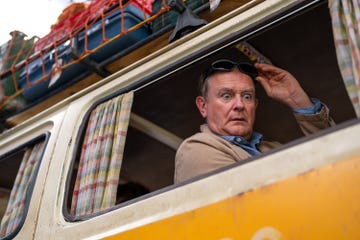 hugh bonneville sitting in a vintage van window wearing sunglasses and gesturing in a still from paddington in peru