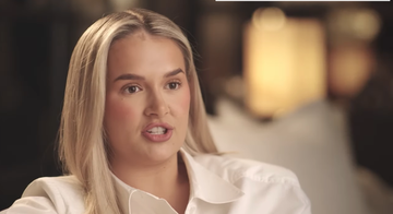 person with long blonde hair wearing a white shirt in a soft dimly lit environment