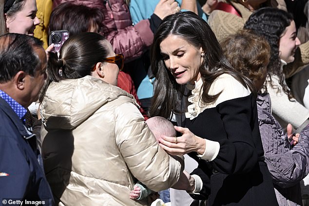 The Spanish monarch cradles a baby held in a mother's arms in the town in south-west Spain