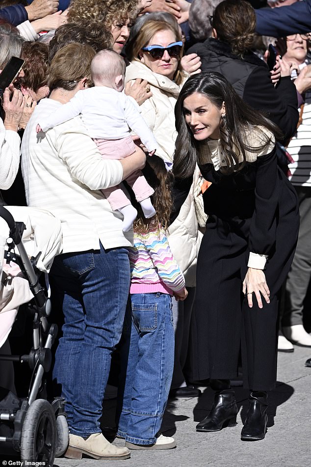 Letizia crouches down to have a one-on-one conversation with an excitable little girl wearing a rainbow cardigan