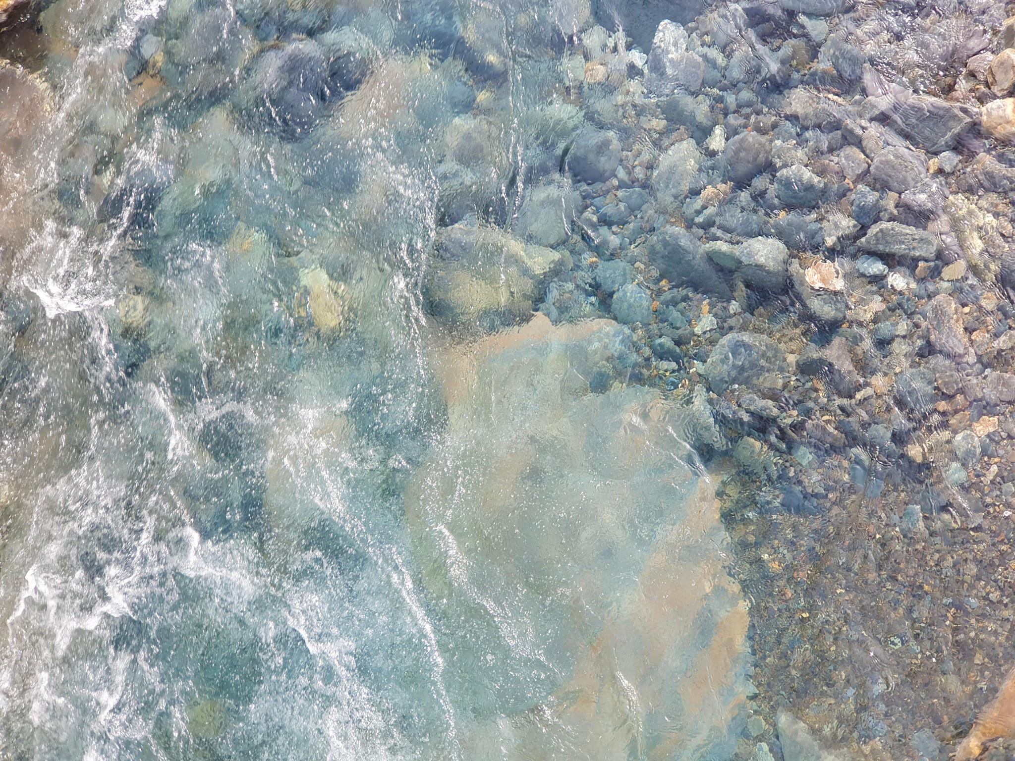 Clear, cold water over smooth river rocks.