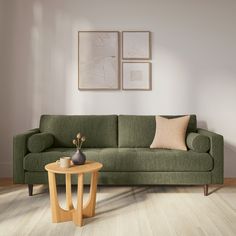 a living room with a green couch and coffee table in front of two pictures on the wall