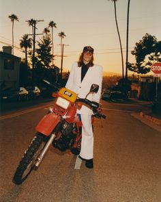 a person standing next to a motorcycle in the street with palm trees behind them and a stop sign